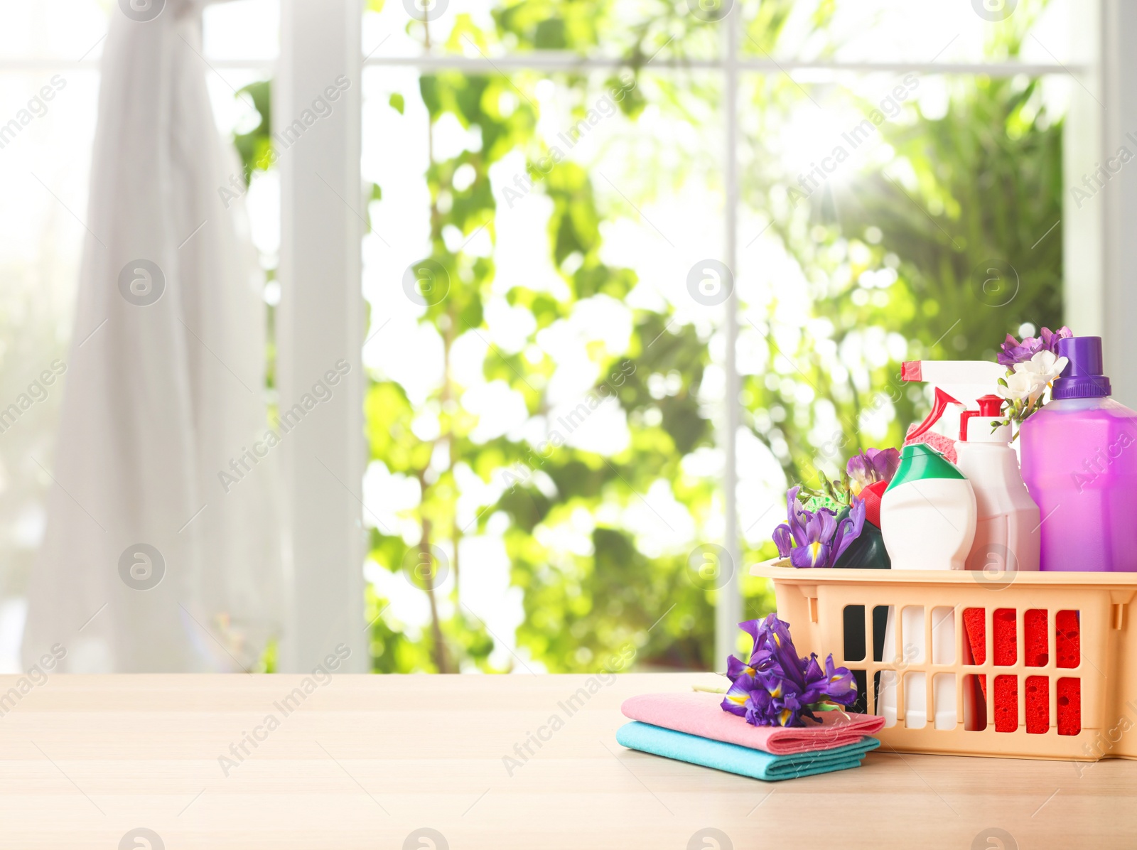 Image of Plastic basket with different detergents on wooden table indoors, space for text. Spring cleaning concept 