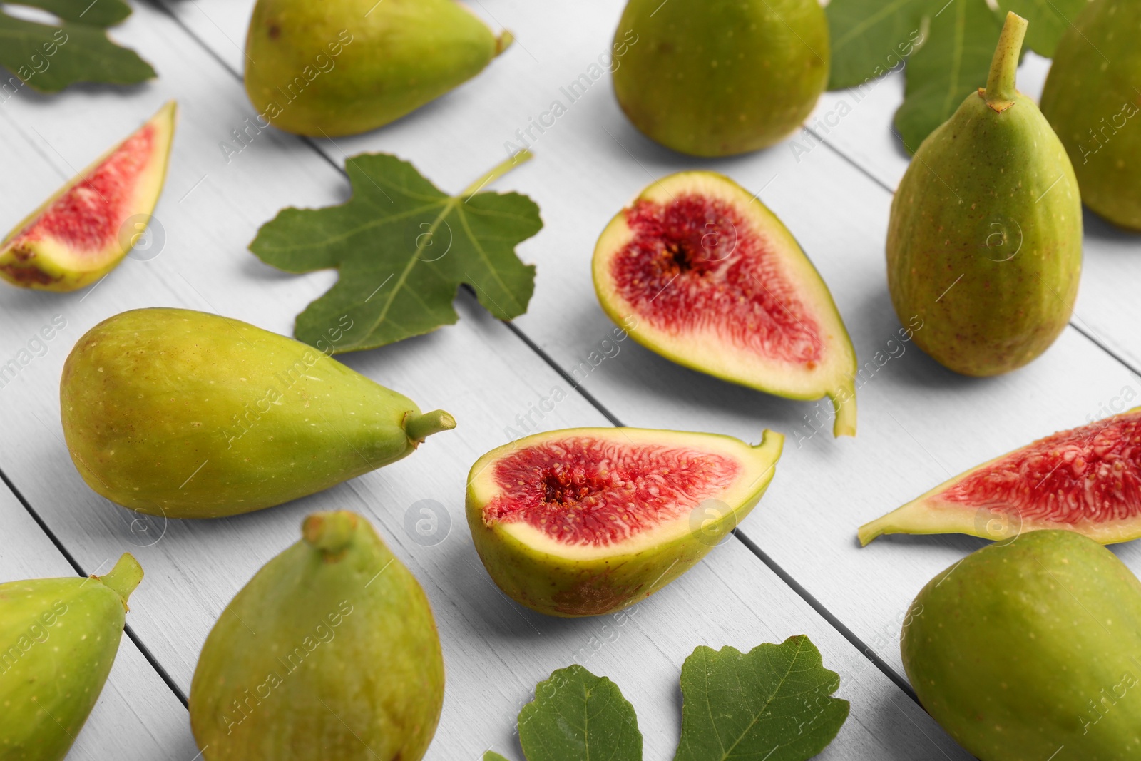 Photo of Cut and whole green figs with leaves on white wooden table, closeup