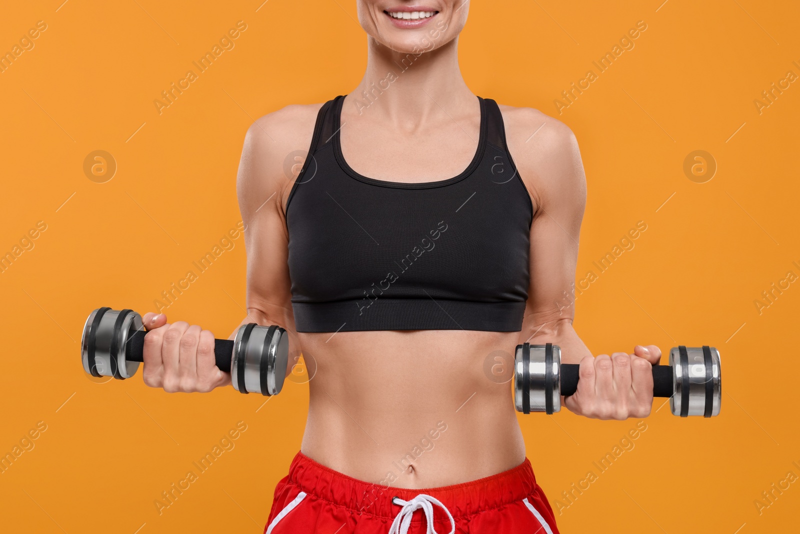 Photo of Happy sportswoman exercising with dumbbells on yellow background, closeup