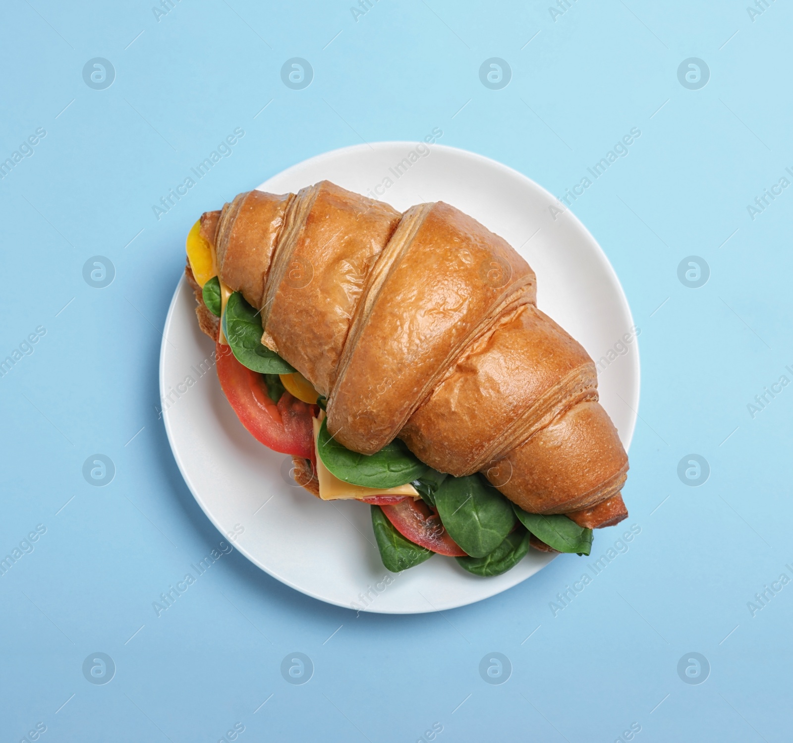 Photo of Tasty vegetarian croissant sandwich on light blue background, top view