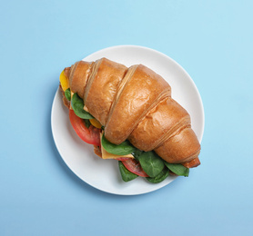 Photo of Tasty vegetarian croissant sandwich on light blue background, top view