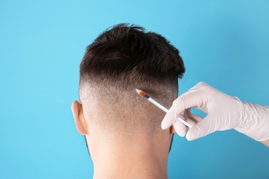 Young man with hair loss problem receiving injection on color background