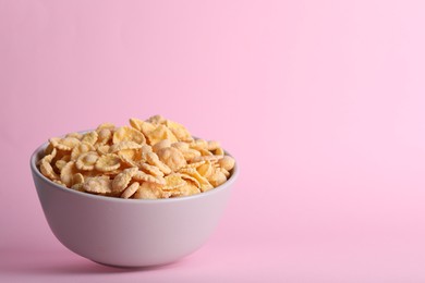 Photo of Bowl of tasty crispy corn flakes on pale pink background, space for text