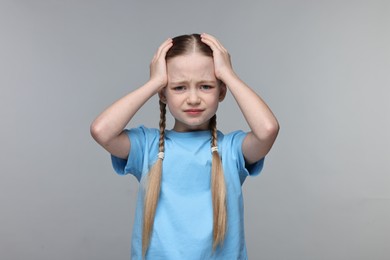 Photo of Little girl suffering from headache on grey background
