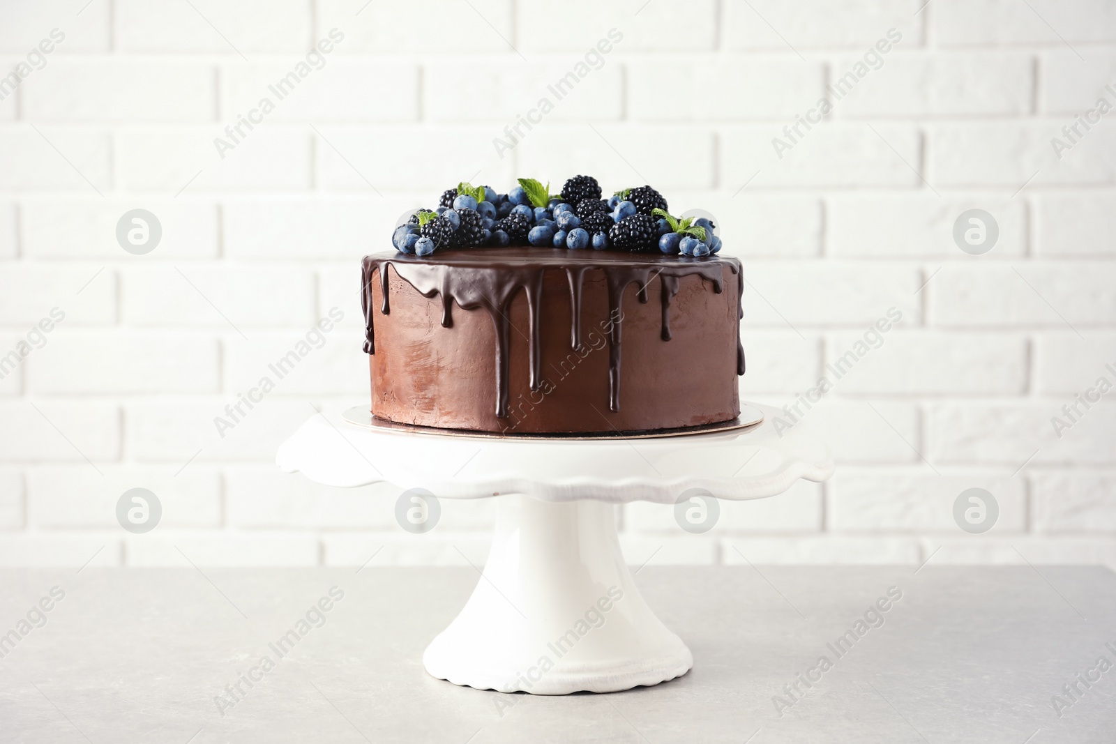 Photo of Fresh delicious homemade chocolate cake with berries on table against brick wall