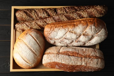 Photo of Basket with different types of fresh bread on black wooden table, top view