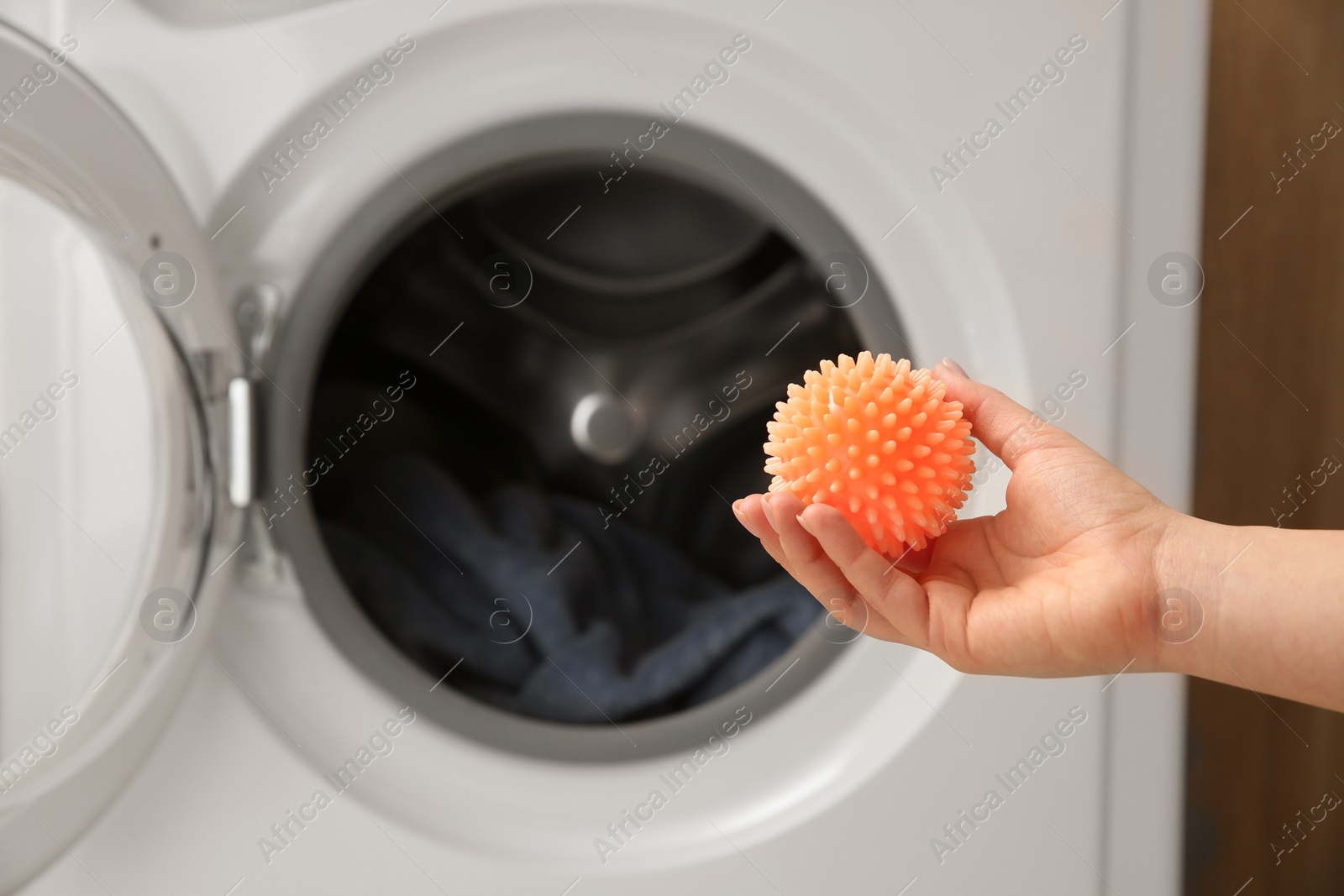 Photo of Woman putting dryer ball into washing machine, closeup