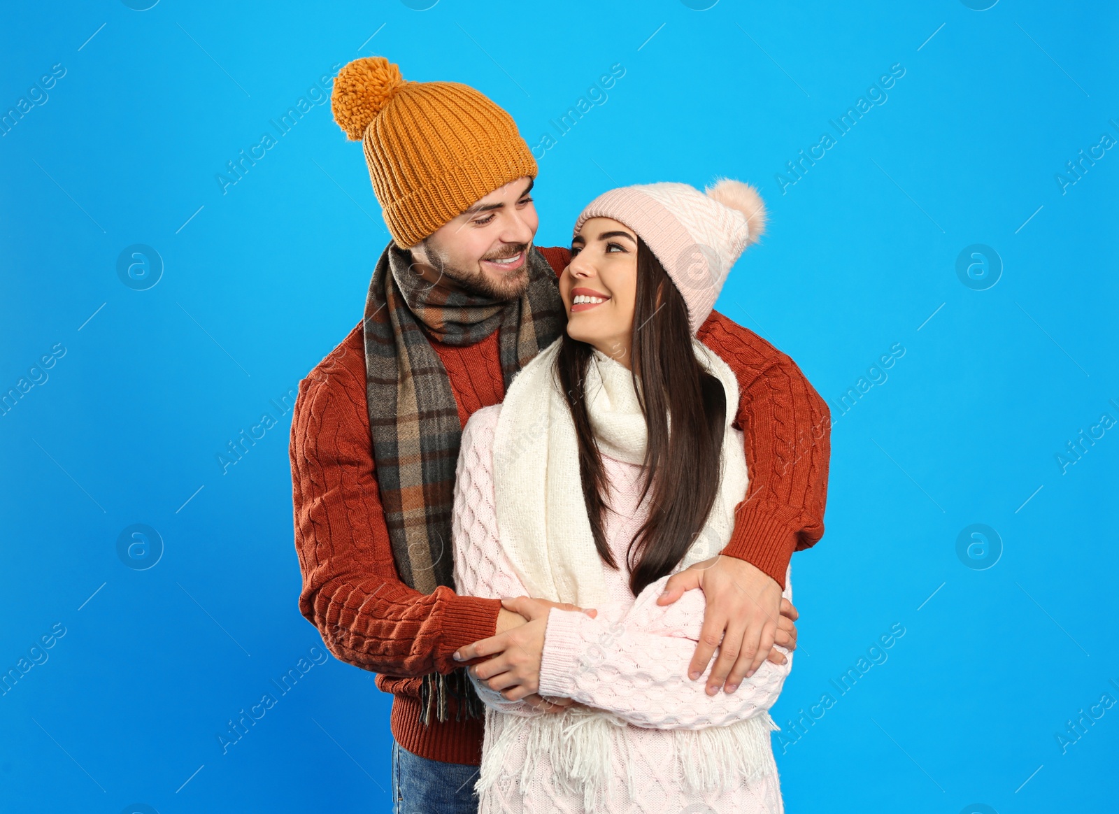 Photo of Happy young couple in warm clothes on blue background. Winter vacation