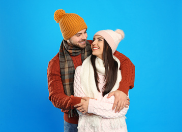 Photo of Happy young couple in warm clothes on blue background. Winter vacation