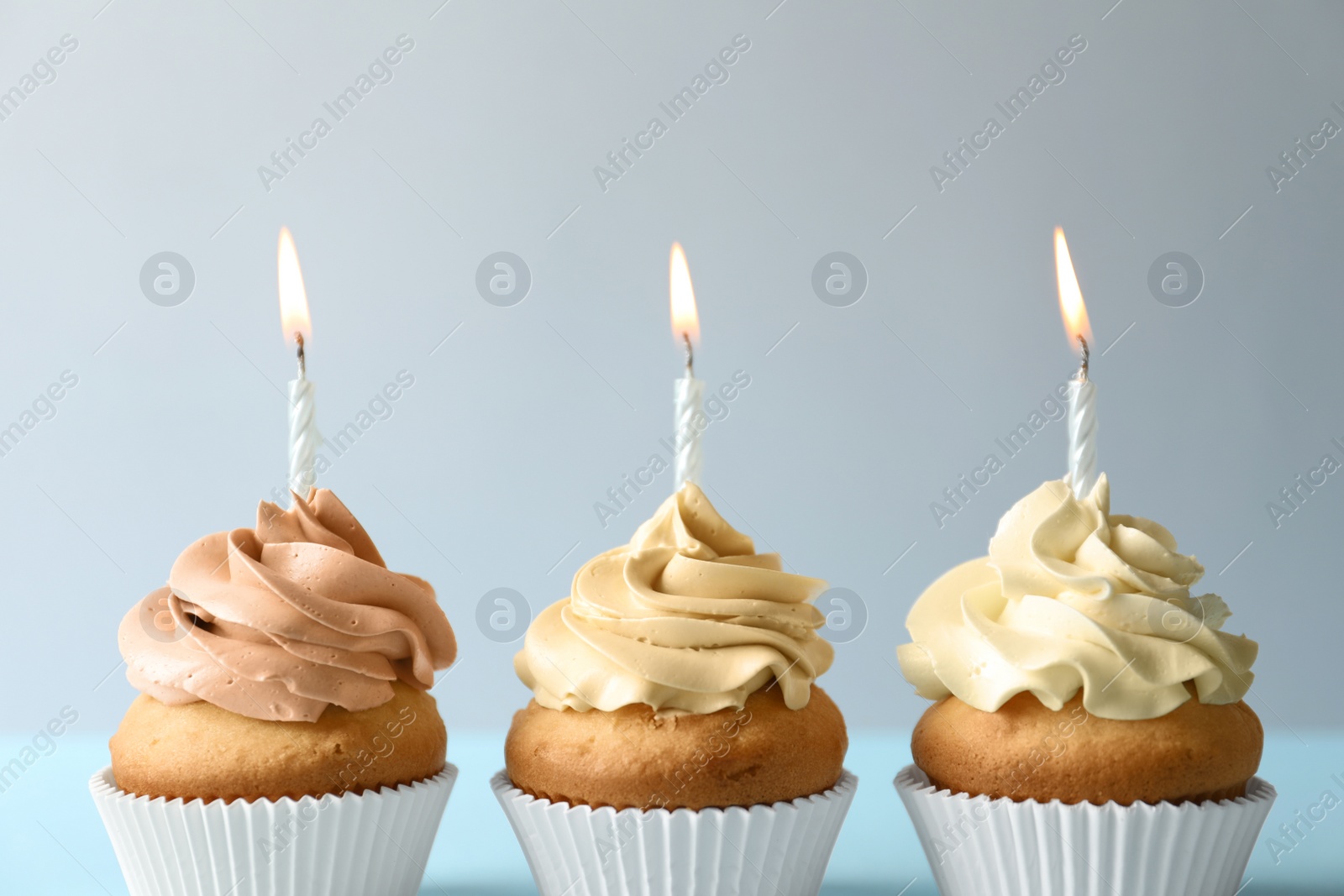 Photo of Delicious birthday cupcakes with candles on light background