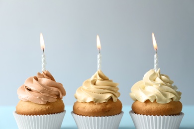 Photo of Delicious birthday cupcakes with candles on light background