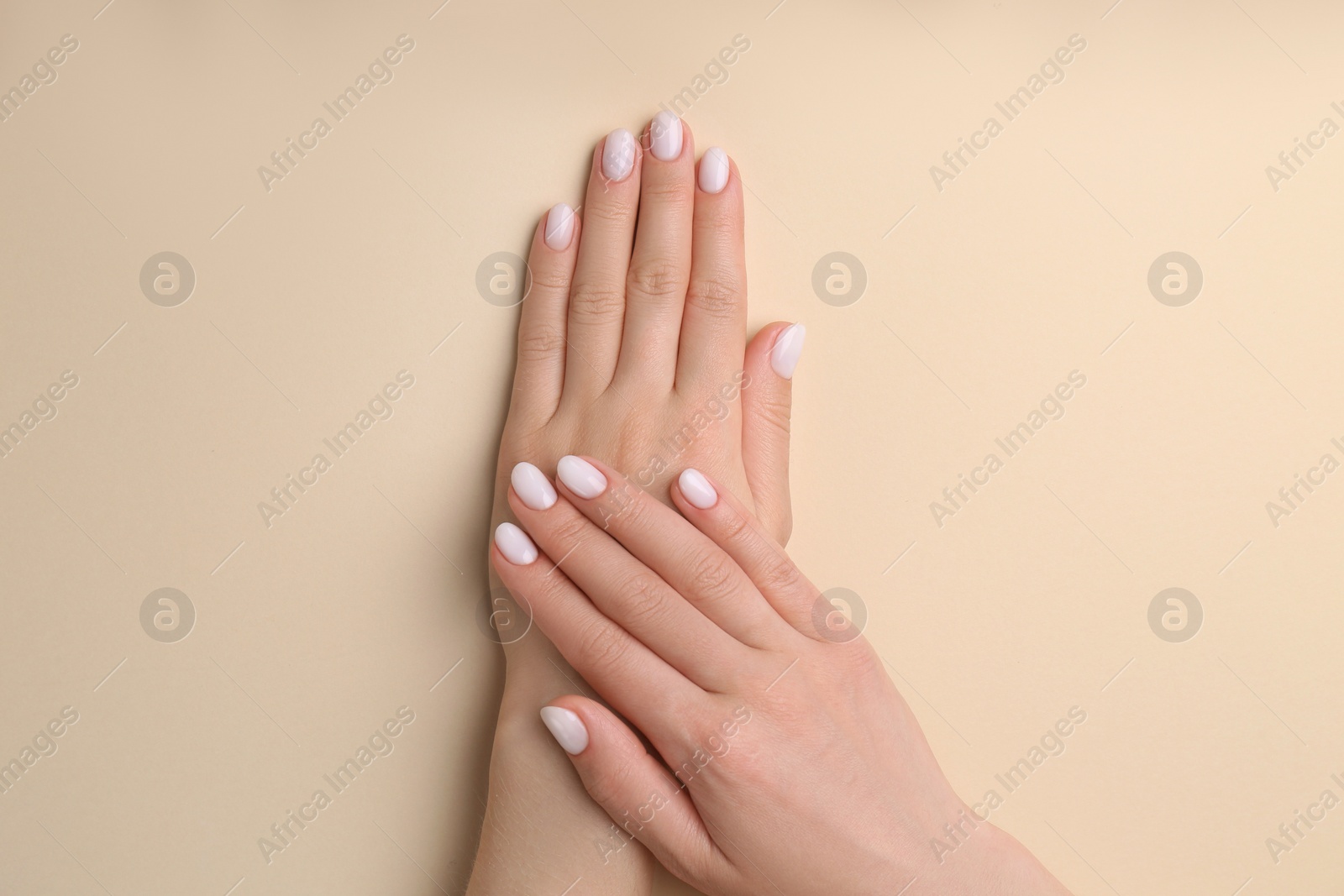 Photo of Woman showing her manicured hands with white nail polish on beige background, top view