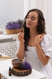 Beautiful young woman with bottle of essential oil at table indoors