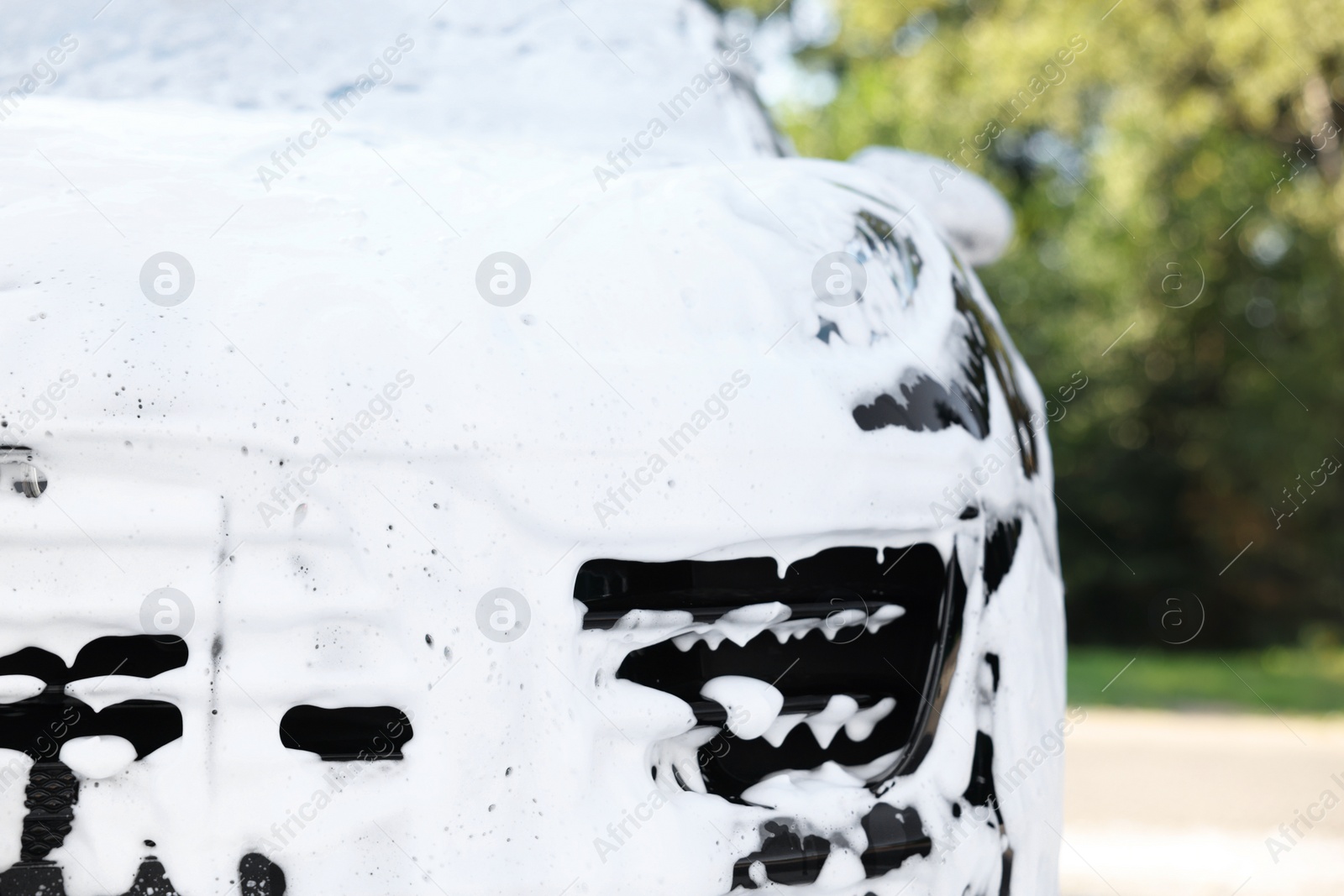 Photo of Auto covered with cleaning foam at outdoor car wash, closeup