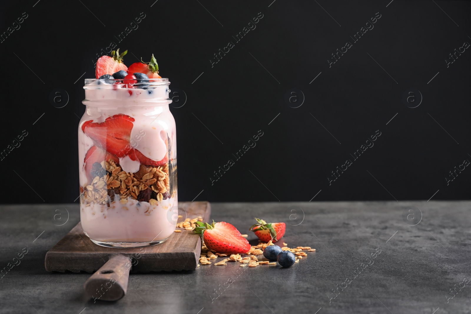 Photo of Mason jar with yogurt, berries and granola on table against black background