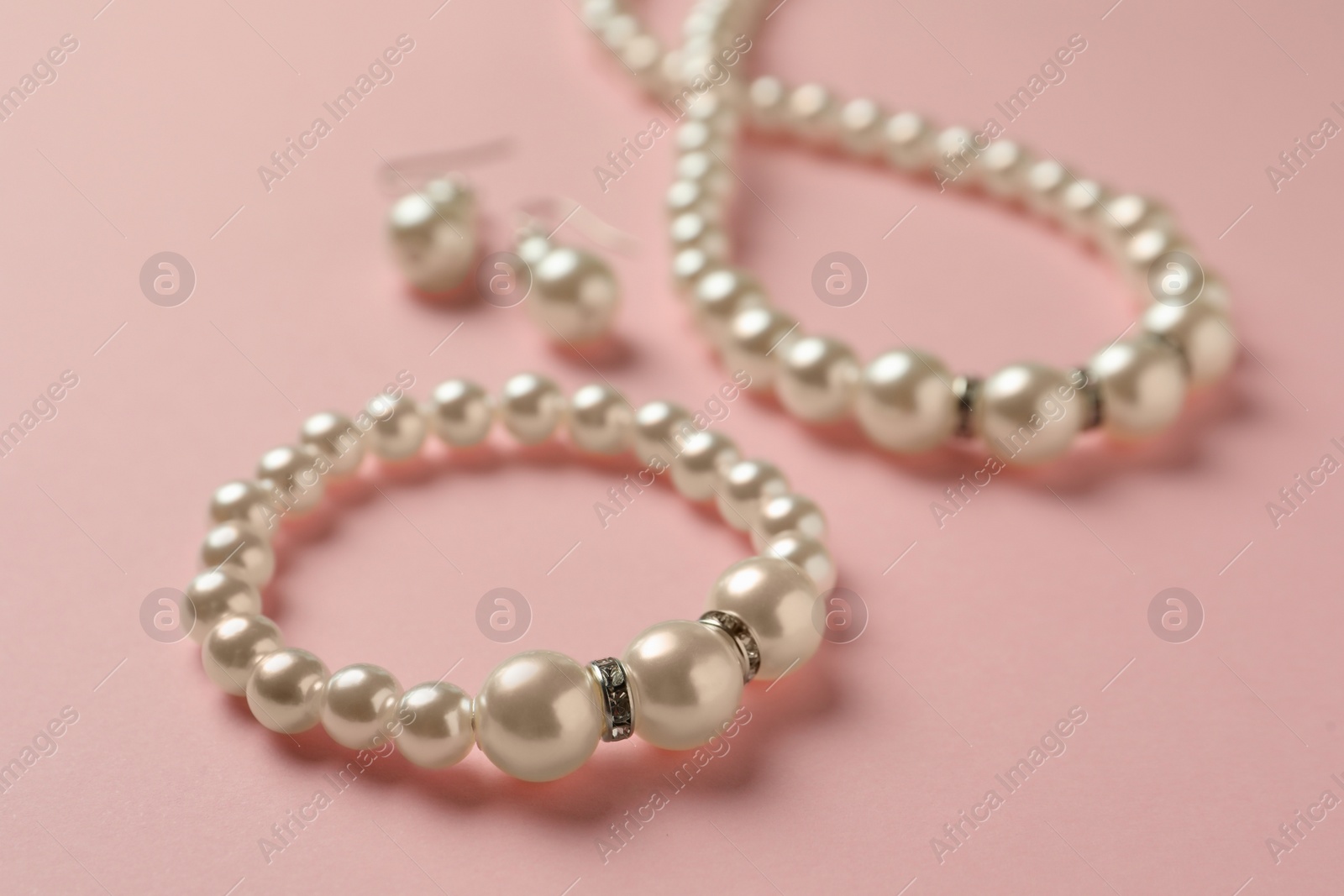 Photo of Elegant necklace, bracelet and earrings with pearls on pink background, closeup