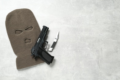 Photo of Beige knitted balaclava, pistol and knife on grey table, flat lay. Space for text