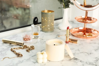 Photo of Burning soy candles, cosmetics and stylish accessories on white window sill indoors