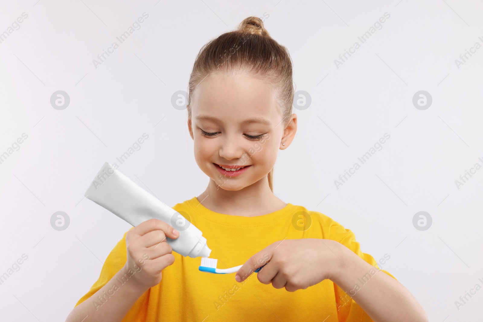 Photo of Happy girl squeezing toothpaste from tube onto toothbrush on white background