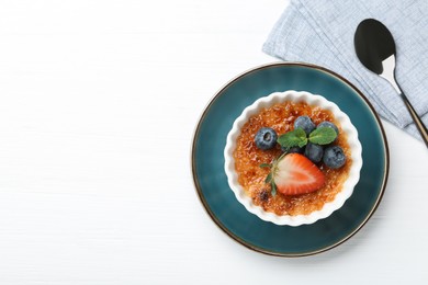 Delicious creme brulee with berries and mint in bowl on white wooden table, top view. Space for text
