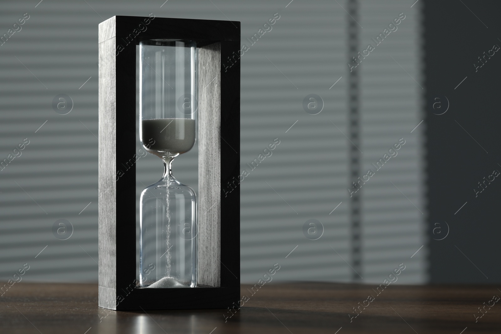 Photo of Hourglass with flowing sand on wooden table, space for text