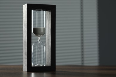 Hourglass with flowing sand on wooden table, space for text