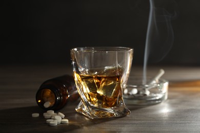 Photo of Alcohol addiction. Whiskey in glass, pills and cigarettes on wooden table