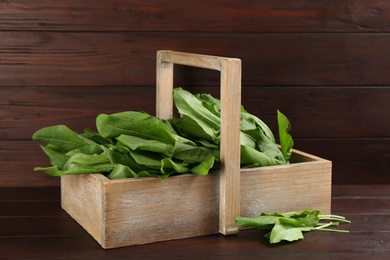 Photo of Fresh green sorrel leaves in crate on brown wooden table