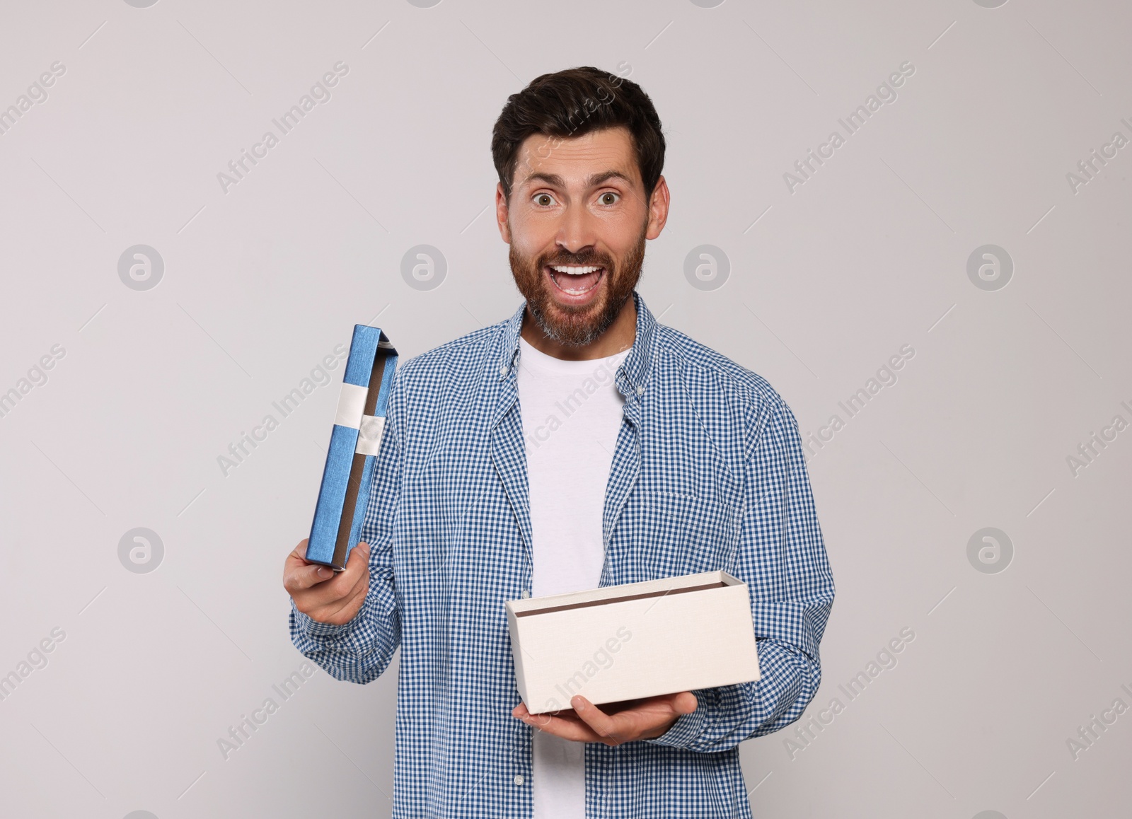 Photo of Emotional man opening gift box on light grey background, space for text