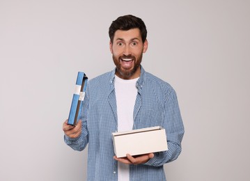 Photo of Emotional man opening gift box on light grey background, space for text