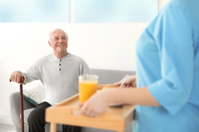 Photo of Nurse serving breakfast to elderly man indoors. Assisting senior people