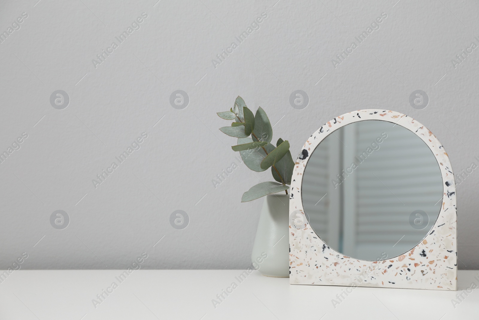 Photo of Stylish round mirror and eucalyptus branch on table near white wall, space for text