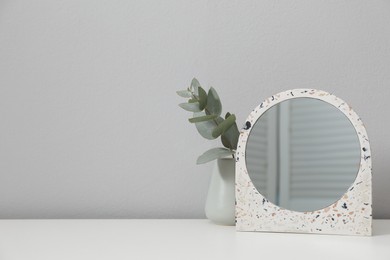 Stylish round mirror and eucalyptus branch on table near white wall, space for text