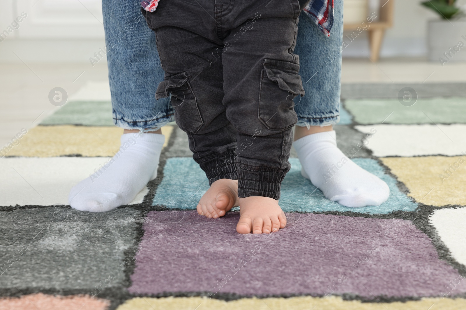 Photo of Mother supporting her son while he learning to walk on carpet indoors, closeup