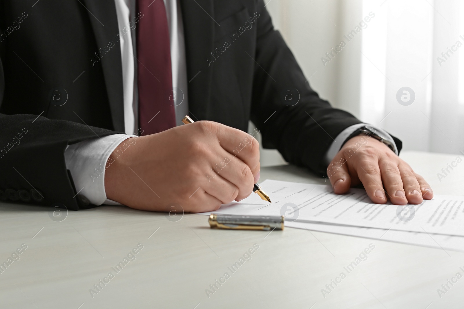 Photo of Notary signing document at wooden table indoors, closeup