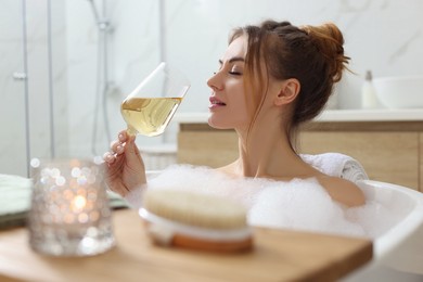 Photo of Beautiful woman with glass of wine enjoying bubble bath at home