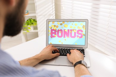 Bonus gaining. Man using laptop at white table indoors, closeup. Illustration of falling coins and word on device screen