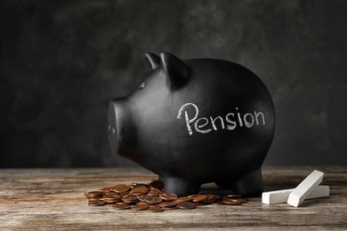 Photo of Piggy bank with word PENSION, chalk and coins on table