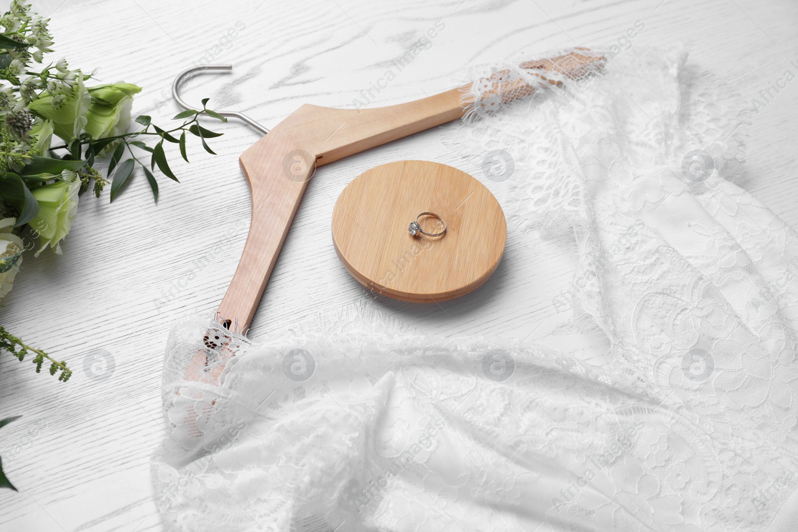 Photo of Beautiful wedding dress, engagement ring and flowers on white wooden background, closeup