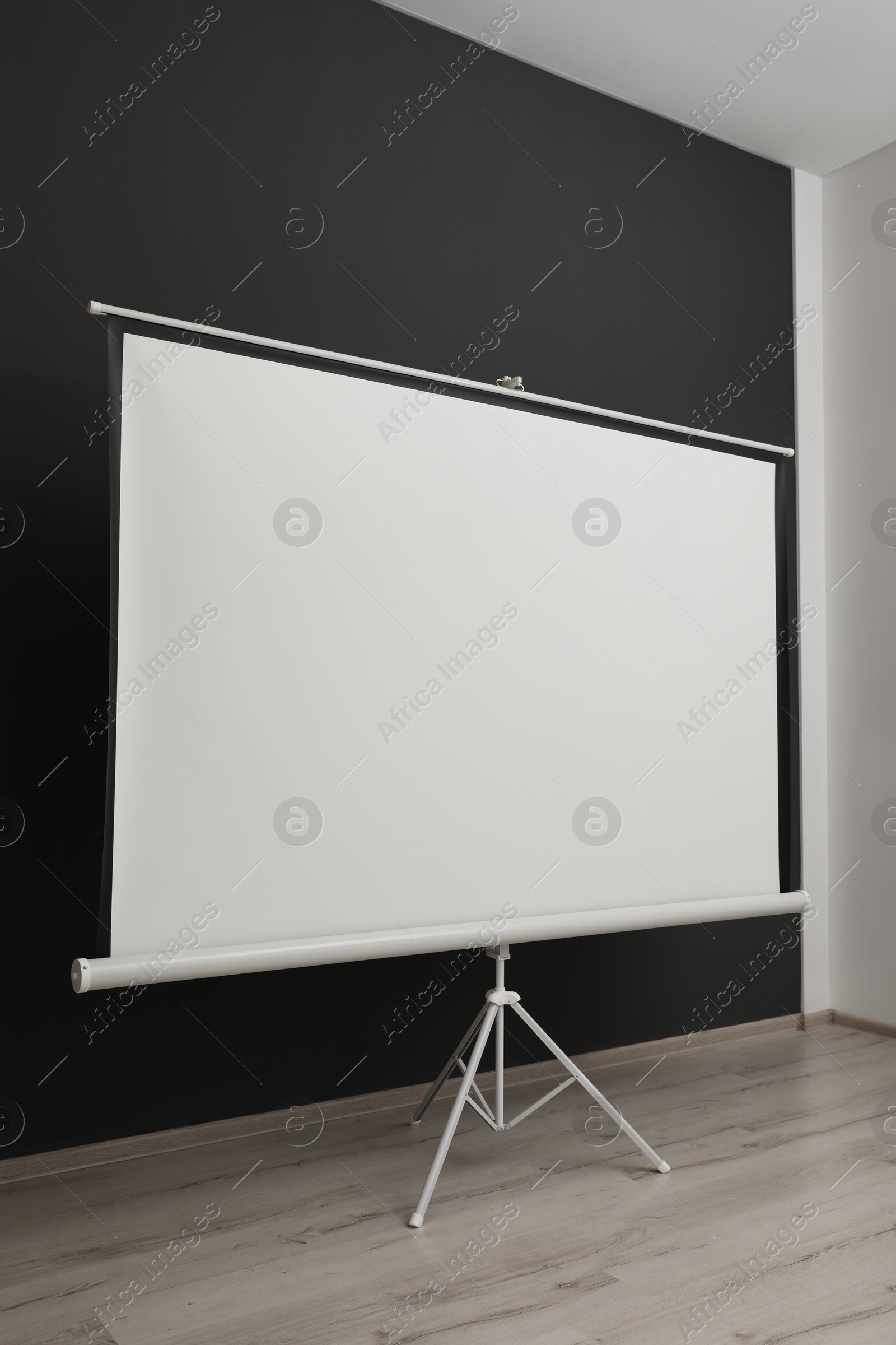 Photo of Blank projection screen near black wall indoors. Space for design