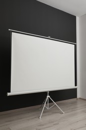 Blank projection screen near black wall indoors. Space for design