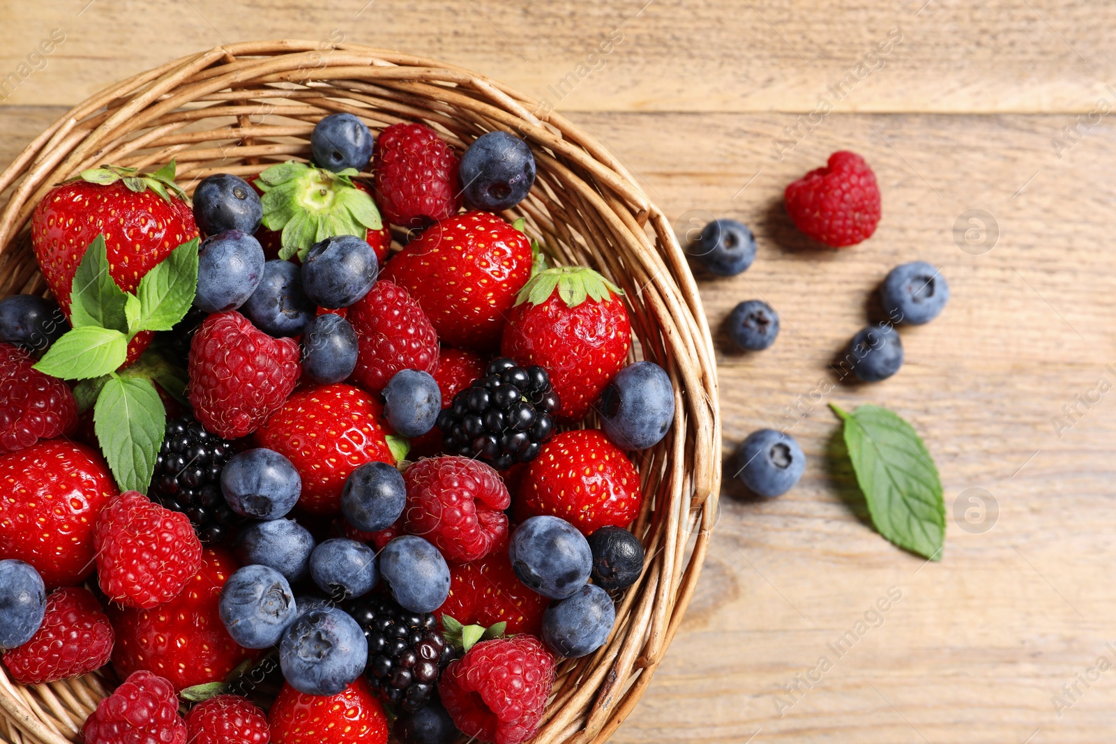 Photo of Wicker basket with many different fresh ripe berries on wooden table, flat lay