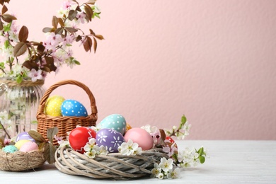 Photo of Composition with painted Easter eggs and blossoming branches on table. Space for text