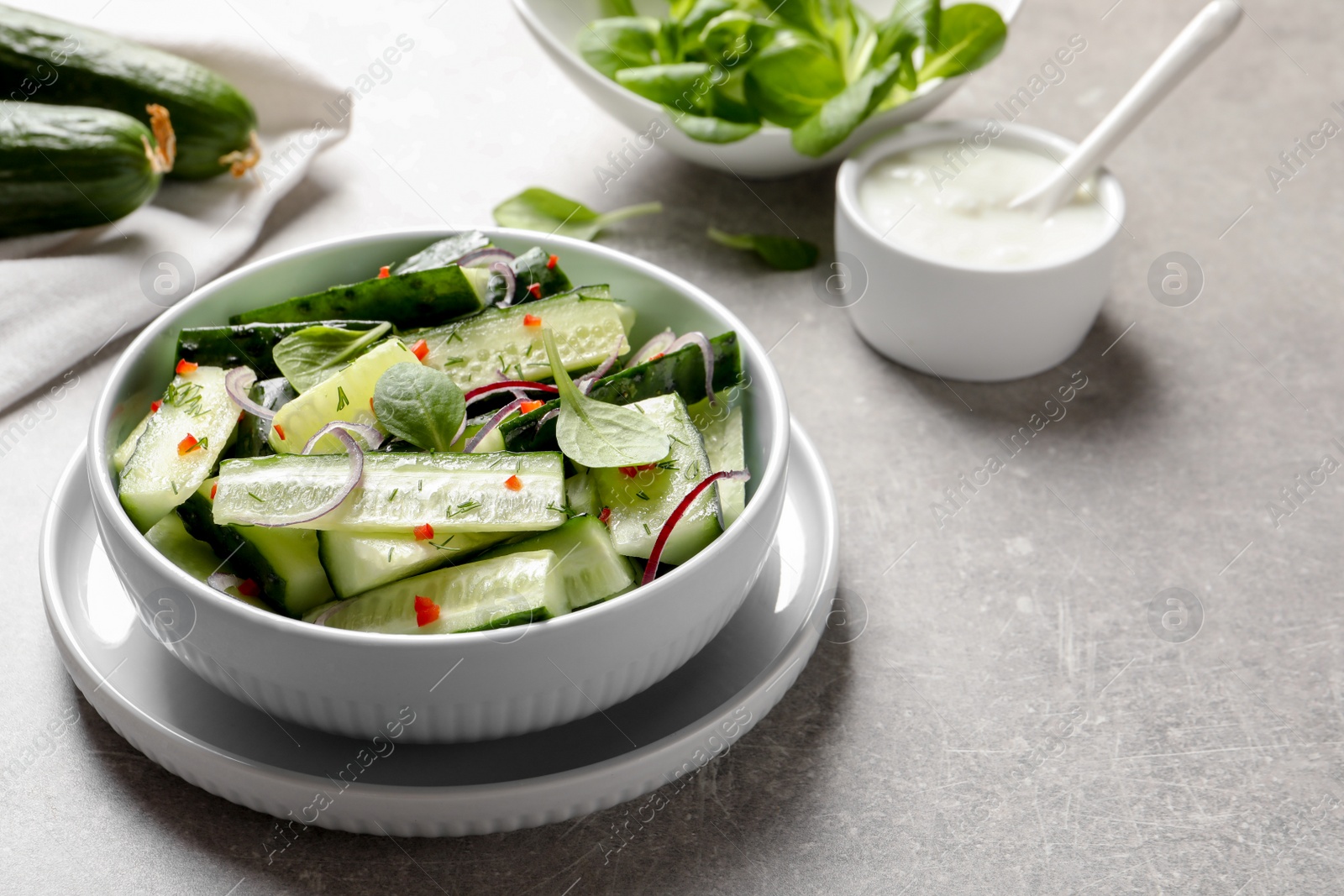 Photo of Delicious cucumber salad with onion and spinach in bowl served on table. Space for text