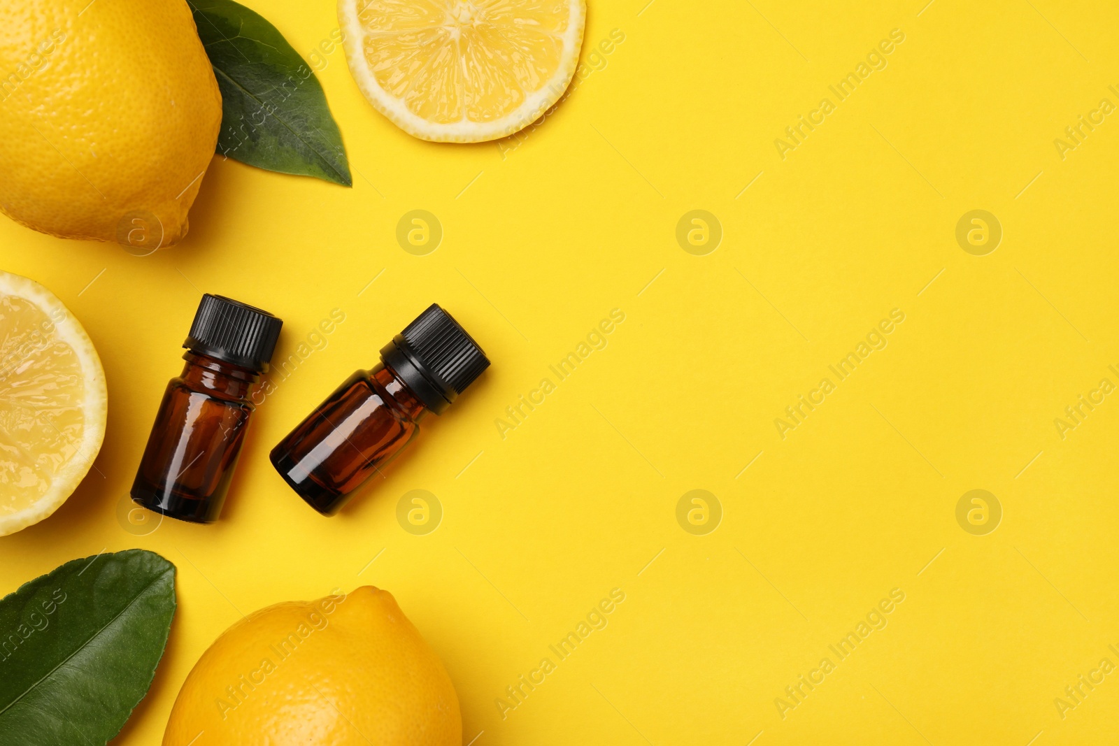 Photo of Bottles of citrus essential oil, fresh lemons and leaves on yellow background, flat lay. Space for text