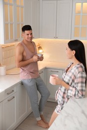 Happy couple wearing pyjamas with cups of coffee in kitchen