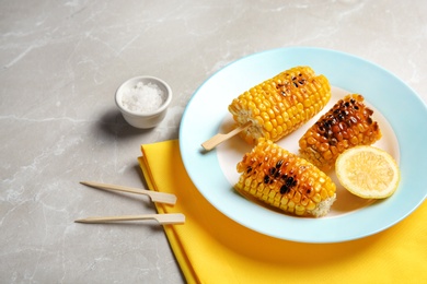 Plate with delicious grilled corn cobs on light table