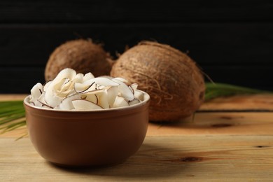 Tasty coconut chips on wooden table against black background. Space for text