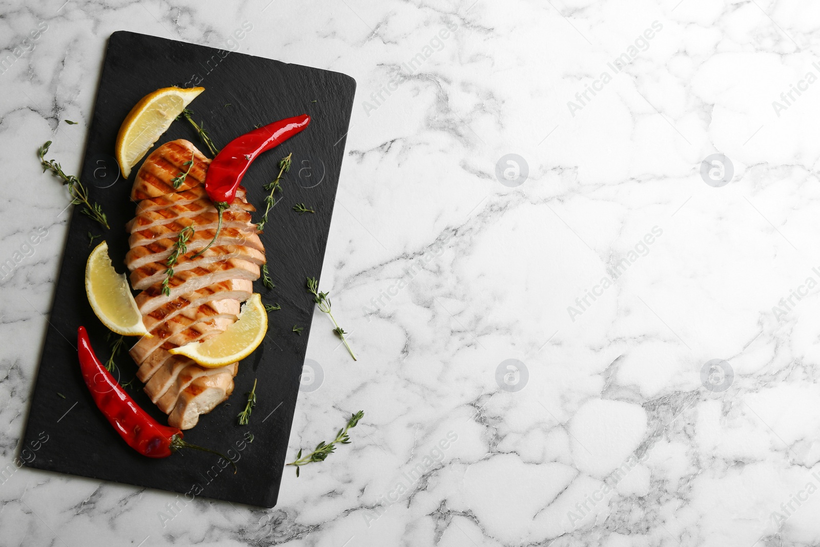 Photo of Tasty grilled chicken fillet with chili peppers and lemon slices on white marble table, flat lay. Space for text