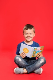 Cute little boy reading book on color background, space for text